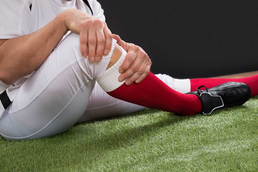 football player holding knee in pain from a sports injury